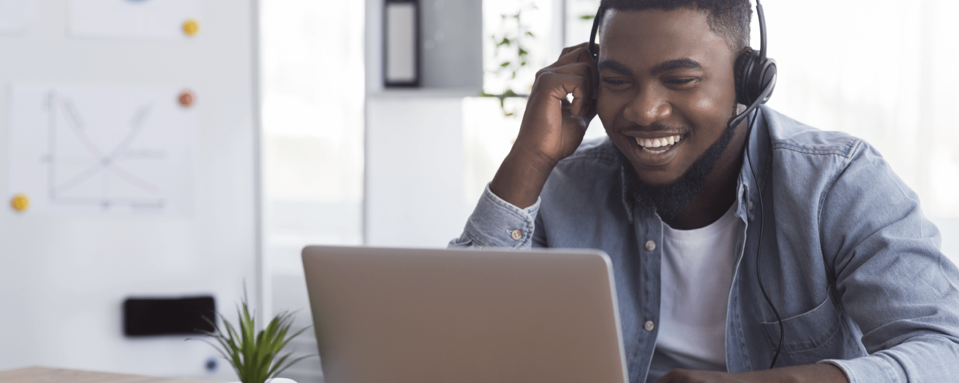 Man sitting at laptop with headphones headset on, smiling and laughing at the screen